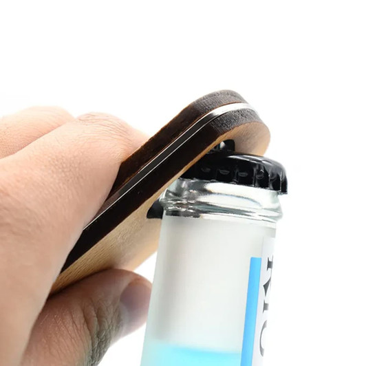 A drink bottle opener key ring made of bamboo, being used to open a bottle, with a black bottle cap visible.