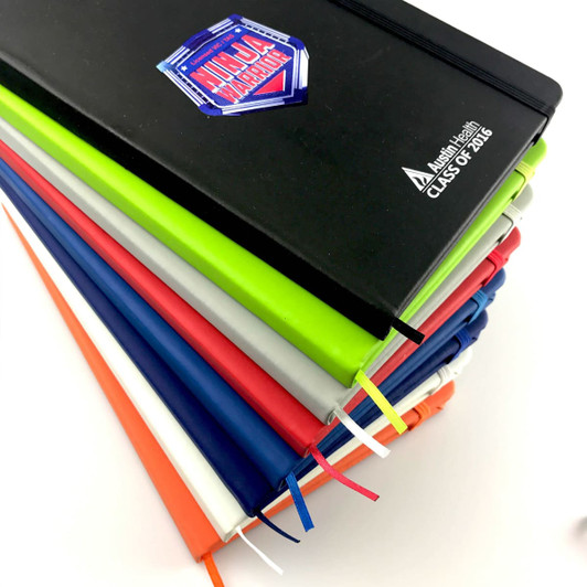 A5 PU notebooks stacked in various colours including black, green, blue, red, orange, and white, featuring a logo.
