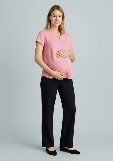 A pregnant woman wearing a pink top and black maternity pants, smiling and posing with hands on her belly.