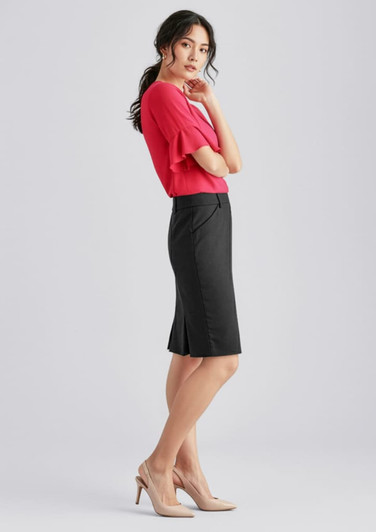 A woman in a red top and black wool stretch multi-pleat skirt stands elegantly, paired with nude heels.