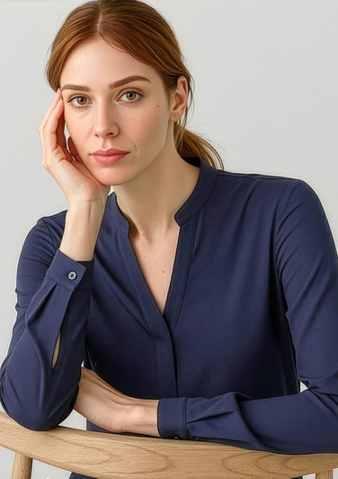 A woman poses wearing a navy long sleeve blouse with a button-up neckline, sitting against a light background.