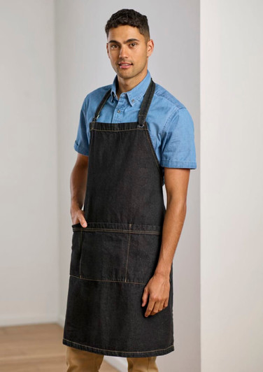 A man wearing a dark denim apron over a blue shirt, featuring pockets and adjustable straps.