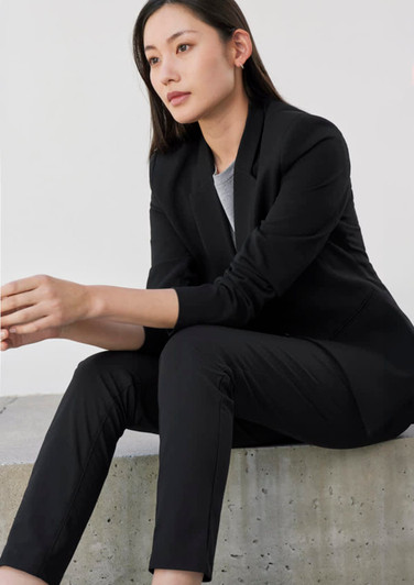 A model wears black Womens Venture Pants paired with a matching blazer, seated against a minimalist backdrop.