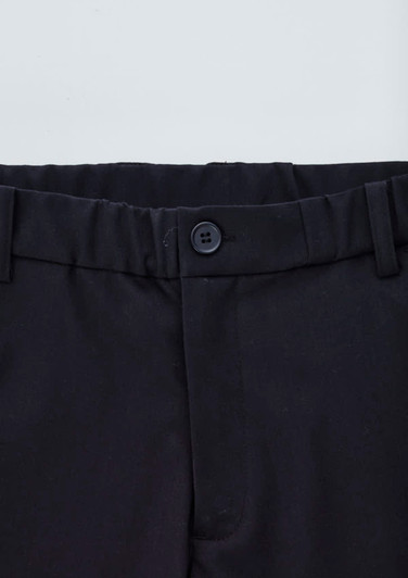A close-up of black cargo pants featuring a button closure and elastic waistband. Logo present.