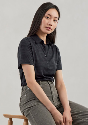 A women's short sleeve polo shirt in a dark colour featuring a subtle textured pattern and buttons, paired with beige trousers.