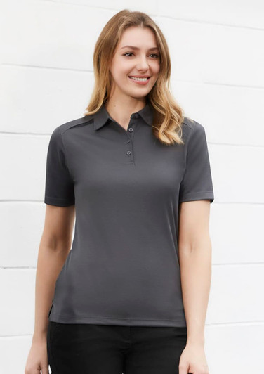 A women's short sleeve polo shirt in dark grey, featuring a collar and a front button placket. It has a logo on the chest.