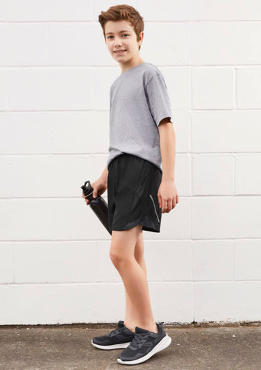 A boy is wearing grey sports shorts and a grey t-shirt, holding a drink bottle. The shorts are black in colour.