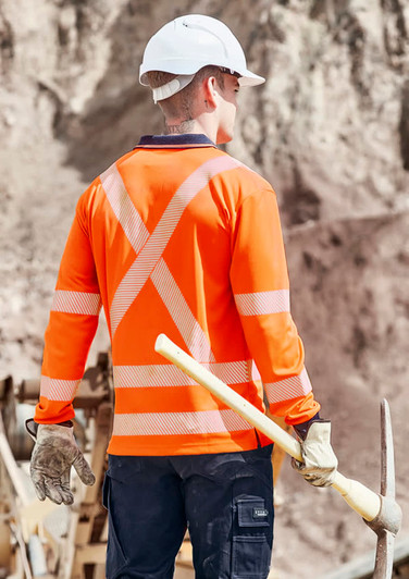 A long sleeve polo shirt in hi-vis orange with reflective stripes, worn by a worker on a construction site.