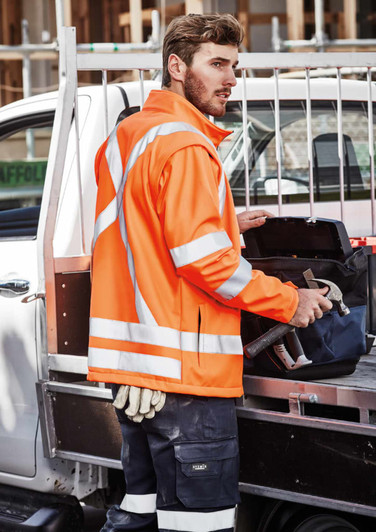 A unisex hi-vis orange softshell jacket with reflective strips, worn by a person holding tools.