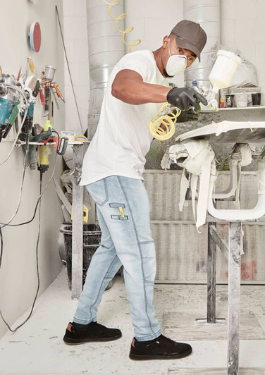 A man wearing light blue stretch jeans and a white t-shirt is spray painting in a workshop.