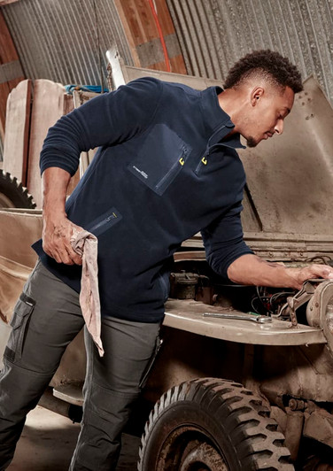 A man in a navy lightweight 1/4 zip polar fleece, working on a vehicle, with a logo on the garment.