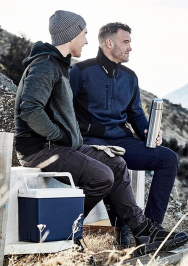 Two men seated outdoors, one wearing a grey reinforced knit hoodie and the other in a navy pullover, holding a drink bottle.