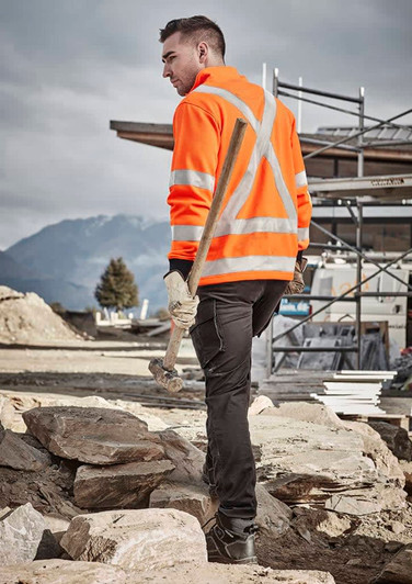 A man wearing an orange high-visibility jumper with reflective stripes, holding a hammer, in a construction setting.