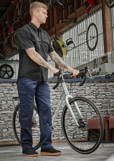 A person wearing navy midweight drill cargo pants and a black shirt stands beside a bicycle in a workshop setting.