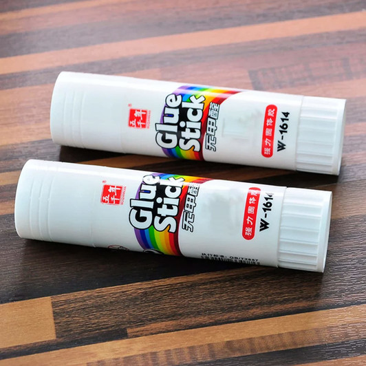 A pair of white glue sticks, each with a colourful logo, resting on a wooden surface.
