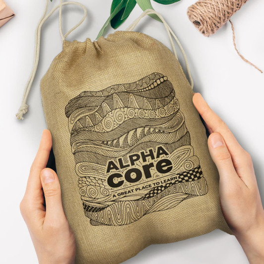 A large jute gift bag featuring decorative patterns and the text "ALPHA CORE - A GREAT PLACE TO LEARN."