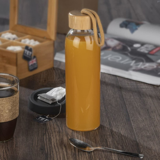 A drink bottle in a clear design with a bamboo lid and a rope handle, filled with orange liquid.