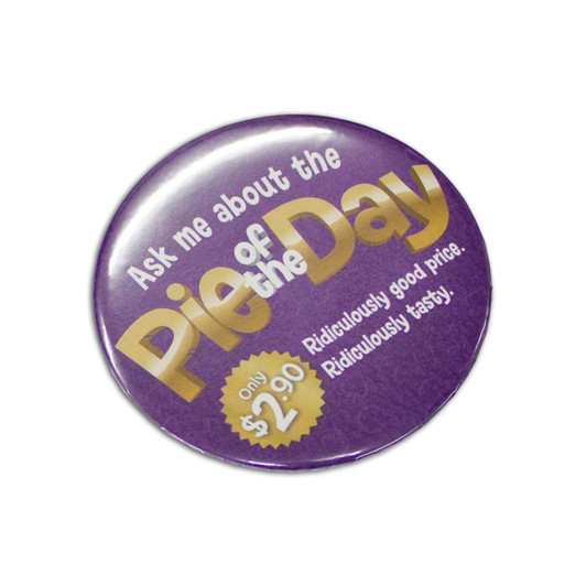 A round 75mm button badge in purple with a shiny finish, featuring a logo and promotional text.