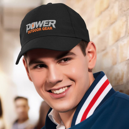 A black cap with an embroidered logo, worn by a smiling person against a brick background.
