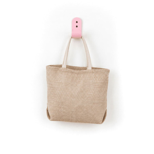 A herringbone jute tote bag in beige with light-coloured handles, hanging on a pink hook.