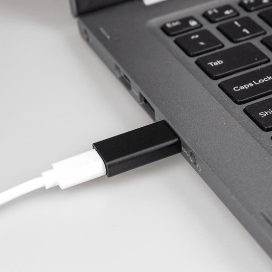 A black USB C adapter connected to a laptop, with a white cable plugged into the adapter.