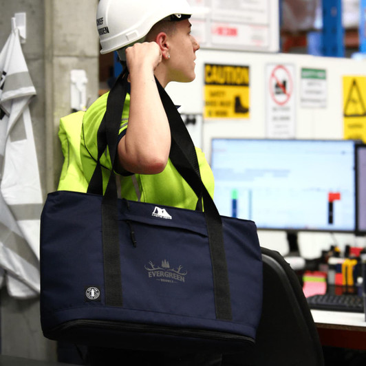 A navy blue tote bag with black straps, held by a person in a safety helmet and high-visibility clothing.