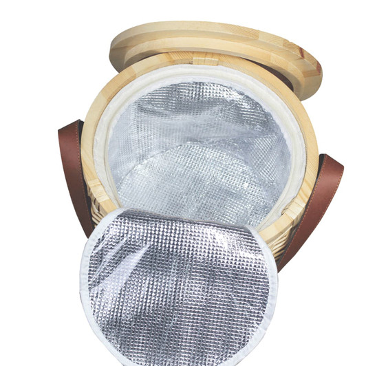 A wicker cooler basket in natural tones with a silver insulated interior and leather straps. It has a round lid.