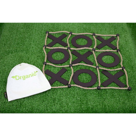 A Tic Tac Toe game with a black grid and wooden pieces, accompanied by a small white, branded bag, set on green grass.