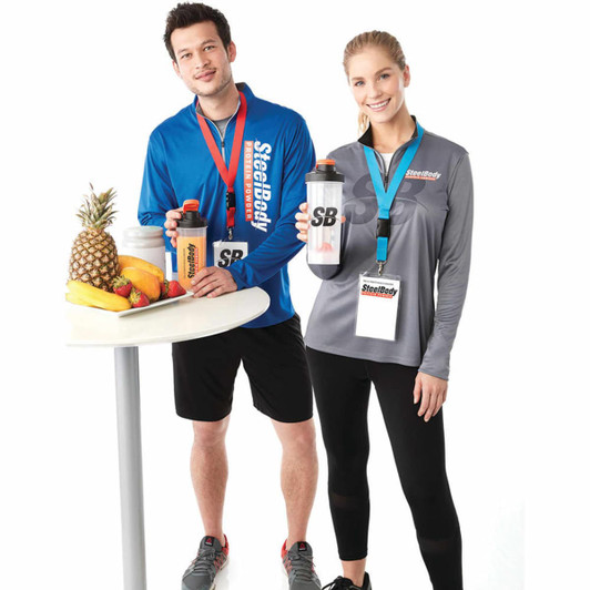 Two individuals wearing long-sleeved track jackets in blue and grey, each holding a drink bottle, standing by a table of fruit.