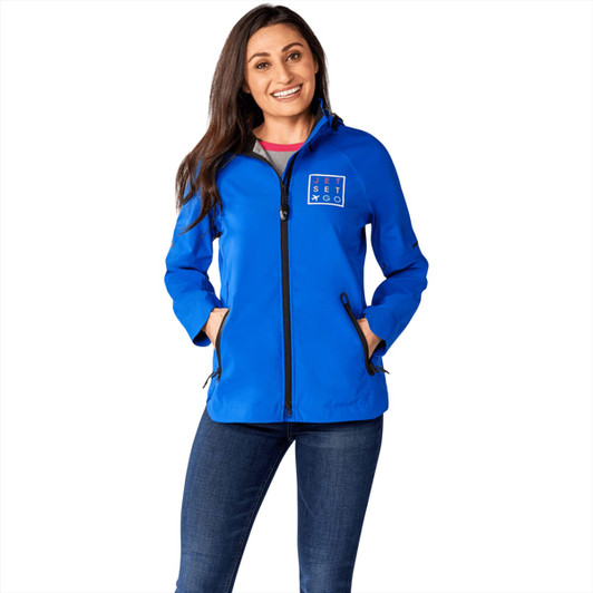 A woman wearing a blue softshell jacket with a logo, featuring a zip front and side pockets.