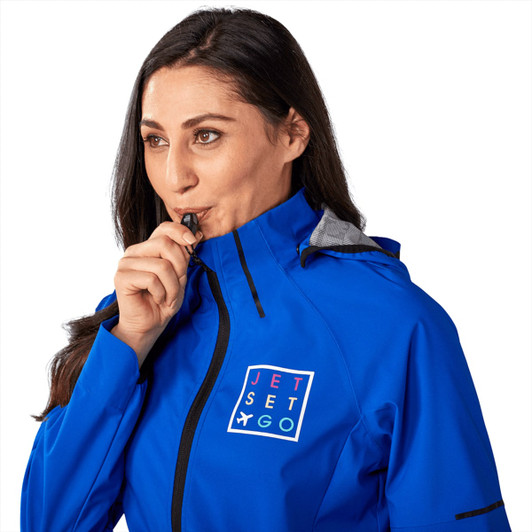 A woman wearing a blue Oracle Softshell Jacket, looking ahead with a whistle in her mouth, featuring a logo.