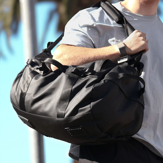 A black duffel bag with sturdy straps and textured detailing, being held by a person.