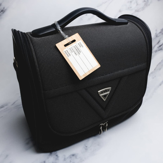 A black luggage tag made from bamboo, attached to a textured black travel bag with a handle.