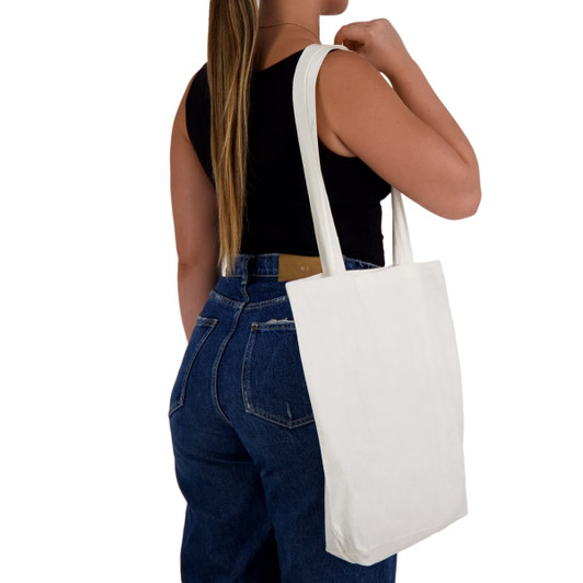 A white tote bag with long handles is being held by a person wearing a black top and blue jeans.