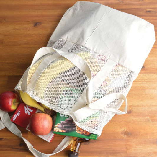 A calico and mesh tote bag filled with fresh apples, a box of cereal, a pack of cookies, and a bunch of bananas.