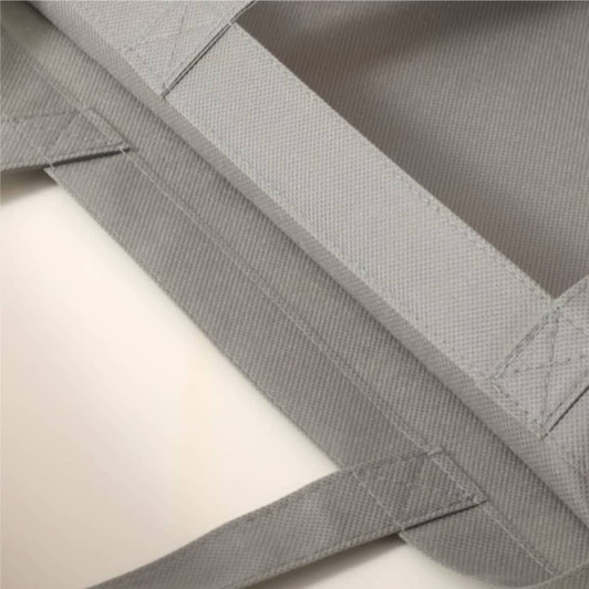 A grey non-woven tote bag with textured fabric and overlocked seams, featuring handles and a logo.