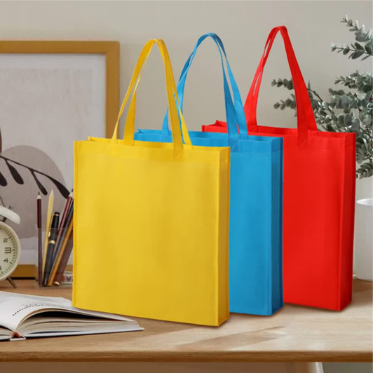 Three tote bags in yellow, blue, and red, featuring handles and a logo, placed on a table with stationery.
