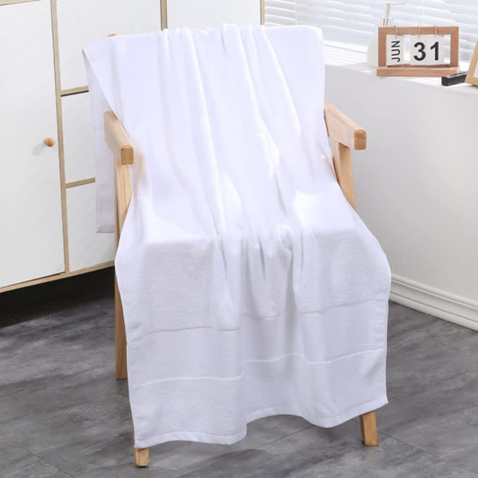 A plush white bath towel draped over a wooden chair, set in a light-filled room with minimal decor.