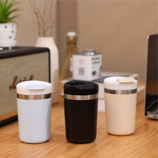 Three coffee mugs in blue, black, and cream, featuring a stainless steel band and a lid, placed on a wooden table.