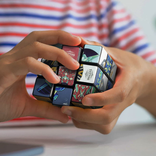 A person holding a colourful custom puzzle cube featuring various designs and a logo.