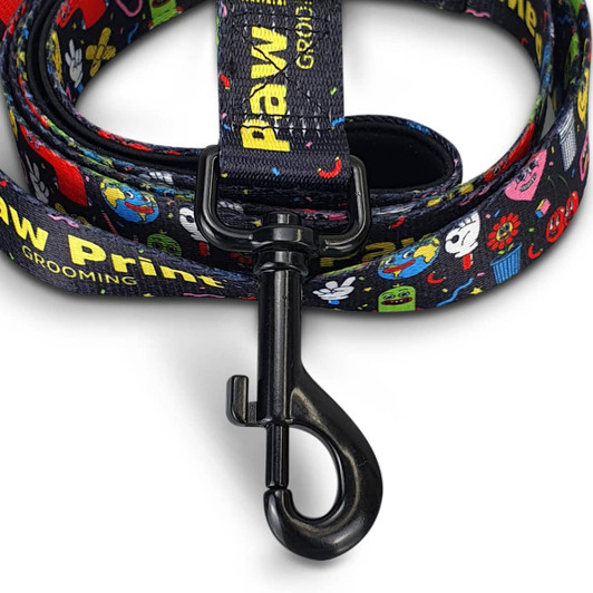 A dog leash featuring a black background with colourful, cartoon-style graphics and a sturdy metal clip.