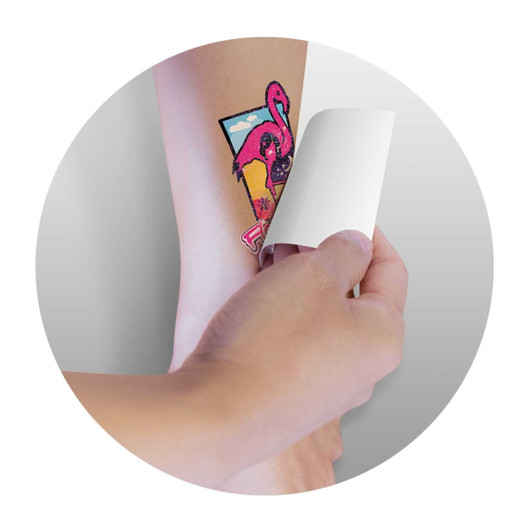 A hand applies a vibrant pink temporary tattoo featuring a flamingo and geometric shapes on skin.
