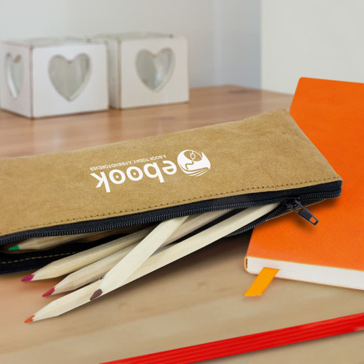 A tan pencil case with a zip, holding coloured pencils, on a wooden surface next to an orange notebook and heart-shaped containers.