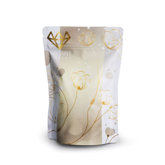A small foil stand-up pouch in white and gold with a floral design and a logo at the top.