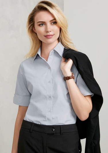 A light grey short sleeve button-up shirt featuring a classic collar, paired with black trousers. It has a logo branding.