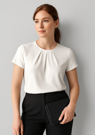 A woman wears a white short sleeve top with a pleat design, paired with black trousers and holding a clutch.