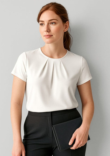 A woman in a white short sleeve top poses against a light grey background, holding a black clutch.
