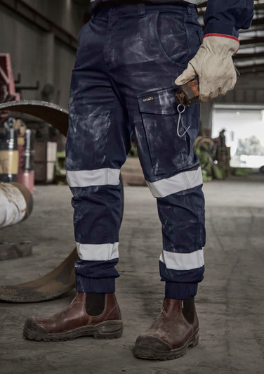 Navy cargo pant with cuffed hems, featuring reflective stripes and multiple pockets, worn with sturdy brown boots.