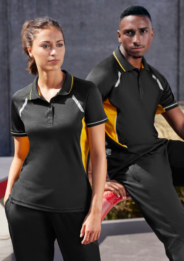 A black and yellow Women's Renegade Short Sleeve Polo, featuring a logo, displayed on a model against an urban backdrop.