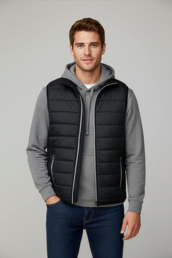 A black puffer vest is worn over a grey hoodie, paired with blue jeans. The model stands against a neutral background.